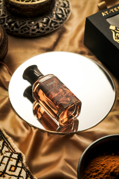 Perfume bottle with black cap and amber glass on a white tray, label reading 1984.
