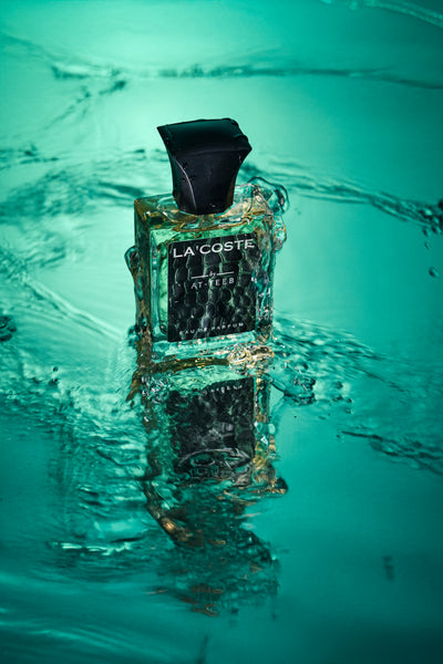 Lacosteé perfume bottle in green-tinted glass with black cap and 'LACOSTE' label