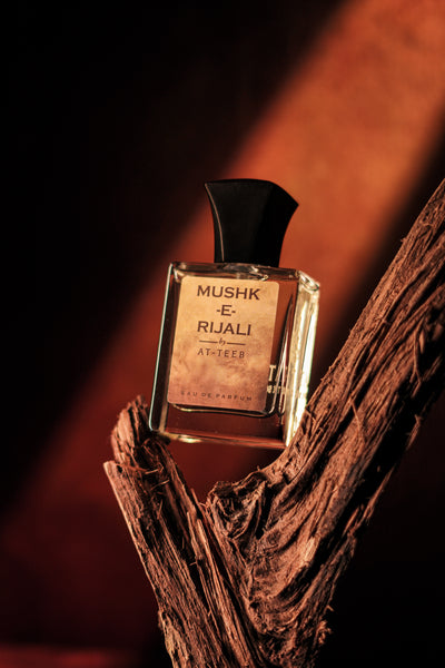 MUSHK-E RIJALI fragrance bottle with black cap, glass perfume vial on wood bark.