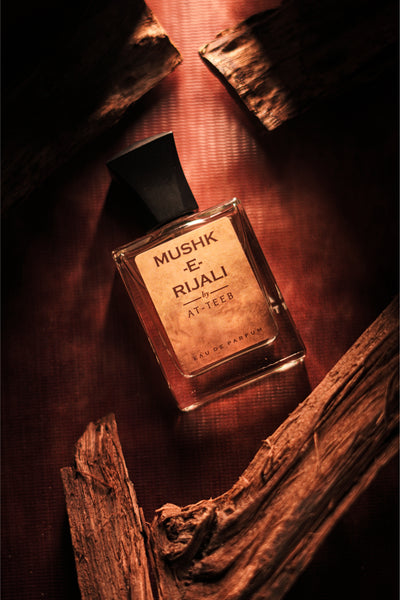 MUSHK-E RIJALI fragrance bottle tilted beside wood sticks and dark cap.