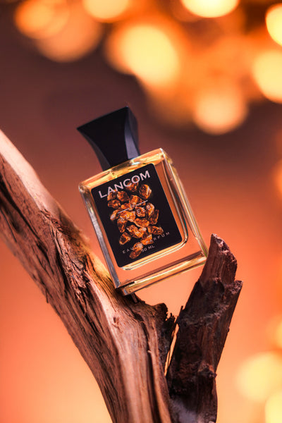 Lancom parfum bottle on dark wooden base, clear glass and black label, angled view